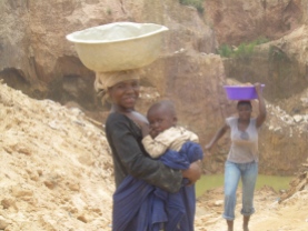 Kleintjes worden op de gebruikelijke Ghanese manier op de rug meegedragen. Moeder houdt even halt op de terugweg terwijl haar teil leeg is, om haar baby de borst te geven.